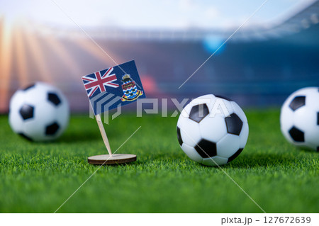 Cayman Islands flag and soccer balls on artificial grass, against blurred stadium backdrop, symbolizing national sport, international football, and championship events 127672639