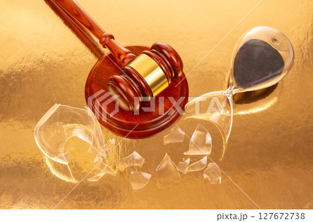 Close-up of a polished gavel next to a broken hourglass with dark sand 127672738