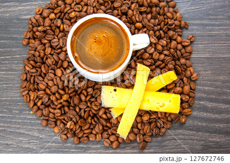 A white cup of espresso sits on a saucer with yellow cheese sticks 127672746