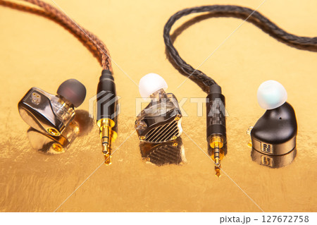 Three earbuds with woven cables and gold-plated jacks on a reflective golden surface 127672758