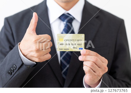 クレジットカードを持ってサムズアップをするスーツ姿のビジネスマン男性 127673765