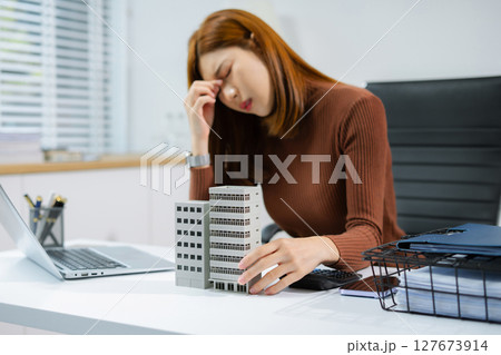 Asian woman stressed over credit card debt, holding bills in frustration. Financial anxiety and economic burden concept in a realistic lifestyle setting. 127673914