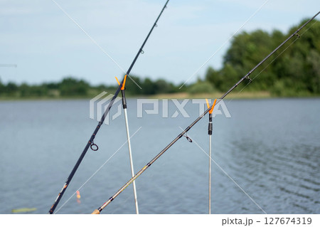 Fishing rod secured by a neon orange holder, set against a backdrop of water and green vegetation. 127674319