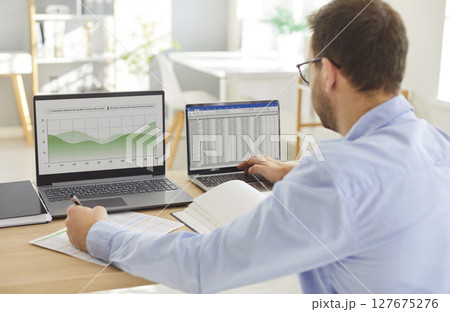 Business man accountant working on a laptop with tables and charts in office Business man accountant working on a laptop with tables and charts in office 127675276