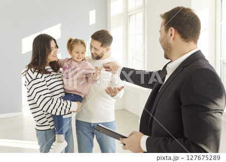 Realtor giving house keys to a happy young family standing in empty new apartment. Realtor giving house keys to a happy young family standing in empty new apartment. 127675289