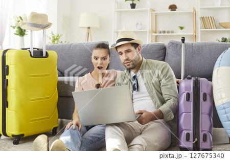 Surprised couple sitting on floor, looking at laptop screen, planning trip shocked by prices. Surprised couple sitting on floor, looking at laptop screen, planning trip shocked by prices. 127675340