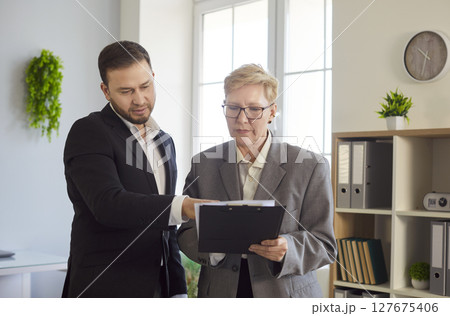 Business people, man and woman looking down at document, focused, serious and engaged in reviewing Business people, man and woman looking down at document, focused, serious and engaged in reviewing 127675406