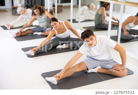 Positive athletic male performing set of exercises on a pilates mat during group class in fitness studio. 127675532