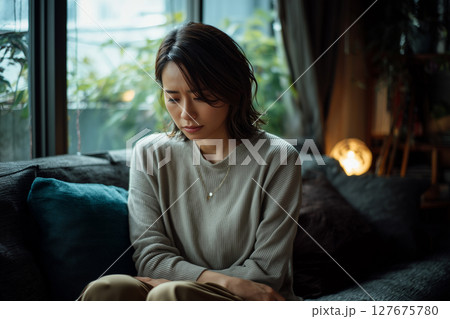 静かな部屋でソファに座りうつむく日本人女性（AI生成画像） 127675780