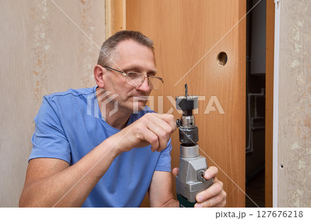 Removing hole saw specialist uses chuck key to loosen drill chuck and release arbor-mounted hole saw after drilling hole for latch installation. Removing hole saw specialist uses chuck key to loosen drill chuck and release arbor-mounted hole saw after drilling hole for latch installation. 127676218
