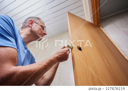 Inserting latch mechanism with attached plate into mortised hole of new interior door to secure locking function and prepare for handle installation by door fitter. Inserting latch mechanism with attached plate into mortised hole of new interior door to secure locking function and prepare for handle installation by door fitter. 127676219