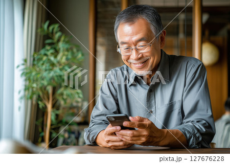 自宅でスマホを楽しむシニア男性（AI生成画像） 127676228