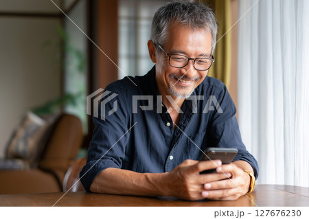 自宅でスマホを楽しむシニア男性（AI生成画像） 127676230