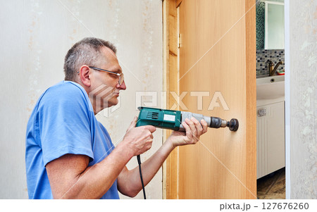 Drilling precise circular hole in wooden door using power drill and hole saw bit to prepare space for installation of lock or door knob hardware. 127676260