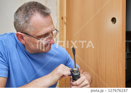 Carpenter uses chuck key to secure spade bit inside drill chuck. Carpenter uses chuck key to secure spade bit inside drill chuck. 127676287