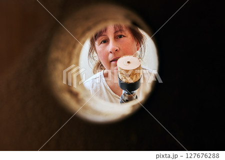 Completing hole cutting woman shows power drill with wood core inside hole saw viewed through circular opening made for latch on wooden door surface. 127676288