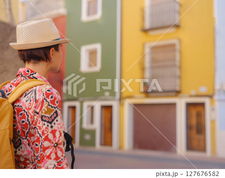 Woman in dress strolls through colorful streets of Spanish coastal town of La Vila Joiosa or Villajoyosa. sunny winter atmosphere highlights charm of Mediterranean architecture and quiet seaside life 127676582