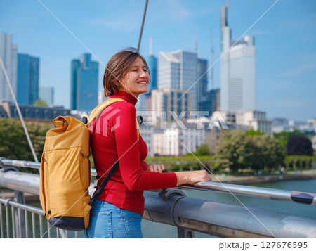Tourist woman explores modern Frankfurt, walking through vibrant streets with contemporary architecture, skyscrapers, and urban spaces, enjoying lively atmosphere of modern side. 127676595