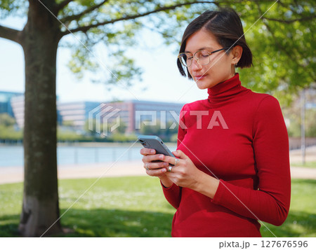 Beautiful woman in walking in Frankfurt on spring day and holding mobile phone. Urban lifestyle concept. Check social networks, send sms or book hotel, exuding confidence and professionalism 127676596