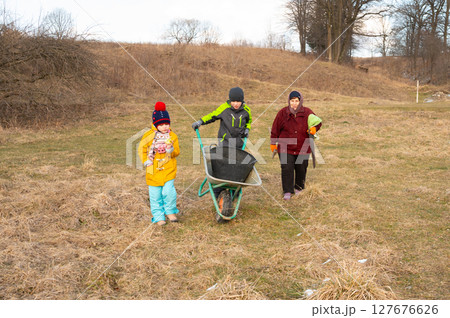 Family members working together in a field during a chilly day, transporting items with a wheelbarrow in a beautiful rural landscape Family members working together in a field during a chilly day, transporting items with a wheelbarrow in a beautiful rural landscape 127676626