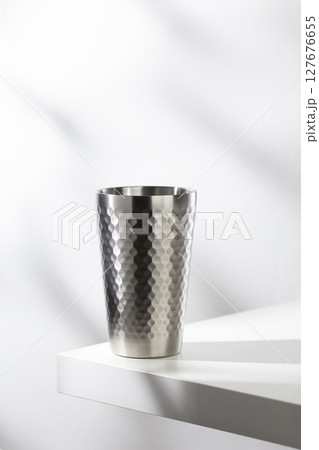Stainless steel glass on a white table with clean, modern lighting. Stainless steel glass on a white table with clean, modern lighting. 127676655