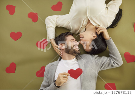 Young man and woman lying on floor with red heart looking at each other and smiling. Couple in love Young man and woman lying on floor with red heart looking at each other and smiling. Couple in love 127678115