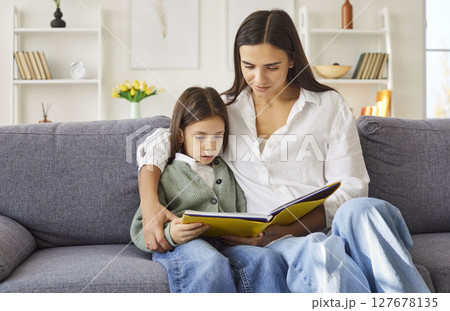 Mother reading a book together with her daughter sitting on sofa at home. Mother reading a book together with her daughter sitting on sofa at home. 127678135
