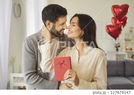 Woman beams with joy as she holds red gift in her hands, celebrating Valentines Day with her man. Woman beams with joy as she holds red gift in her hands, celebrating Valentines Day with her man. 127678147