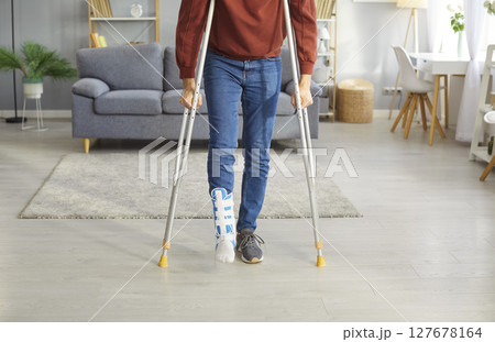 Young man with broken leg after accident using crutches standing at home with plastered leg. 127678164