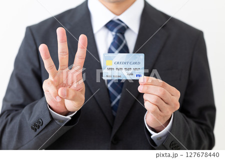 クレジットカードを持って3本指を立てるスーツ姿のビジネスマン男性 クレジットカードを持って3本指を立てるスーツ姿のビジネスマン男性 127678440