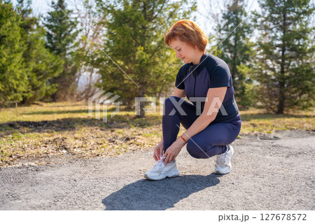 Woman tying shoelaces before going for a run outdoors. Fitness preparation, motivation, and healthy lifestyle routine. 127678572