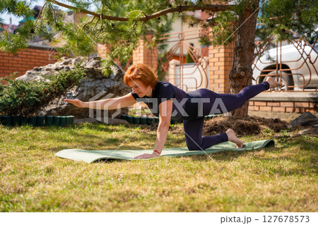 Woman doing stretching exercises on a mat in the park with focus on spine and mobility. Gentle fitness, body awareness, and healthy movement routine. 127678573