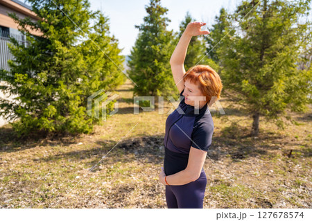 Woman stretching outdoors in a park during early morning exercise. Healthy routine, body mobility, and active lifestyle in nature. 127678574