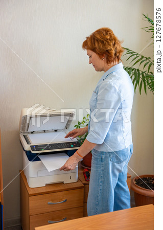 Woman copying documents using an office printer in a realistic administrative workspace. Paperwork routine, clerical tasks, and everyday office operations Woman copying documents using an office printer in a realistic administrative workspace. Paperwork routine, clerical tasks, and everyday office operations 127678576