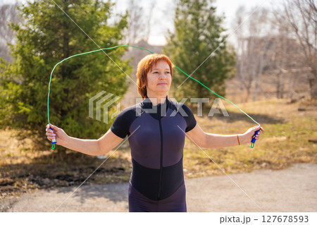 Woman jumping rope during morning workout in a green park. Cardio training, coordination, and energetic outdoor lifestyle. 127678593