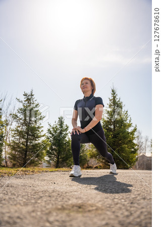 Woman stretching outdoors in a park during early morning exercise. Healthy routine, body mobility, and active lifestyle in nature. 127678610