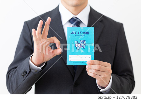 お薬手帳を持つスーツを着たミドル男性ビジネスマン 127678882
