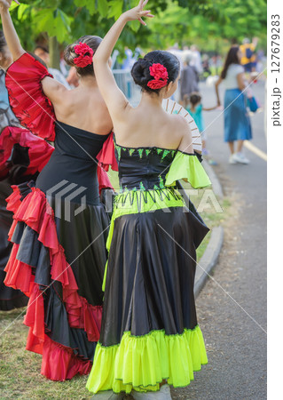 Flamenco dancers in vibrant dresses with red flowers walking in city park with traditional moves at outdoor festival in park. Concept of flamenco, cultural performance, Spanish Cultural Festival Flamenco dancers in vibrant dresses with red flowers walking in city park with traditional moves at outdoor festival in park. Concept of flamenco, cultural performance, Spanish Cultural Festival 127679283