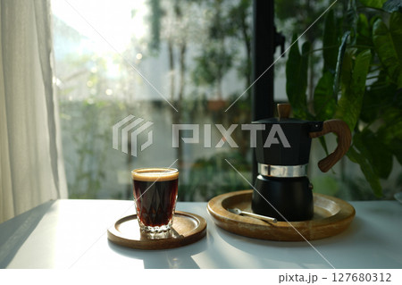Coffee and black moka pot on white table by the window Coffee and black moka pot on white table by the window 127680312