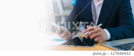 Businessman uses phone and a stylus on tablet at desk with a laptop and copy space , Modern remote work, digital productivity, technology integration, Efficient multitasking in a professional setting. 127680432