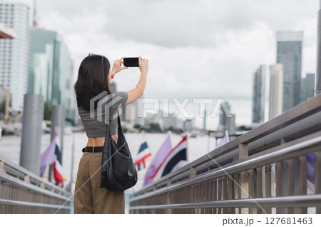 Solo southeast asian woman teenager blogger world travel explorer take photo smartphone express local cultural experience tourism concept wait boat Chao Phraya river Bangkok Thailand asia 127681463