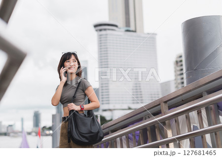 Solo southeast asian woman teenager blogger world travel tourism Bangkok Thailand express joy to friend smartphone. Wait for Chao Phraya river boat for local cultural experience. Asia explorer 127681465
