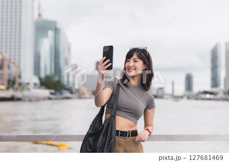 Solo Southeast Asian woman teenager blogger world travel. Local cultural tourism experience concept for explorer Bangkok Thailand. Express joy with smartphone, wait for friend boat Chao Phraya 127681469