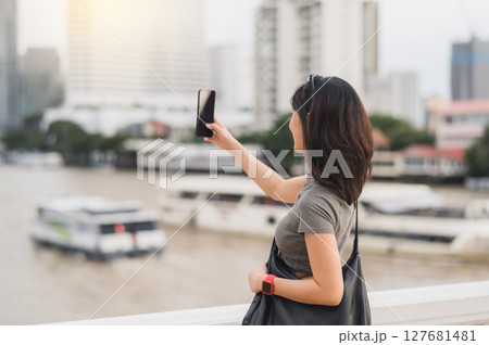 Solo southeast asian woman teenager blogger on world travel tourism. happy explorer take photo with smartphone of boat on Chao Phraya River. Local cultural experience in Bangkok Thailand Asia 127681481