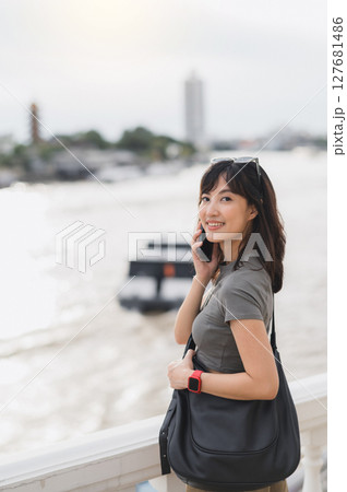 Happy solo Southeast Asian woman on world travel tourism in Bangkok Thailand. great local cultural experience for young explorer using smartphone near boat on Chao Phraya river Happy solo Southeast Asian woman on world travel tourism in Bangkok Thailand. great local cultural experience for young explorer using smartphone near boat on Chao Phraya river 127681486