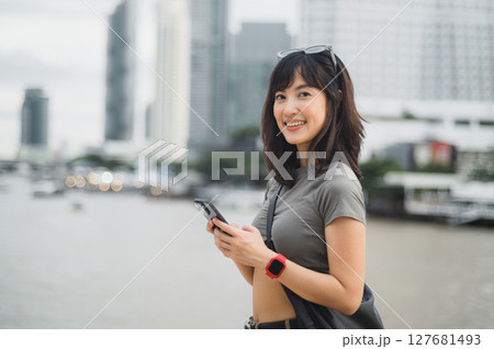 Happy young southeast asian woman teenager blogger using smartphone for searching travel guide. World explorer enjoying local cultural experience. Asia tourism concept Chao Phraya River Bangkok 127681493