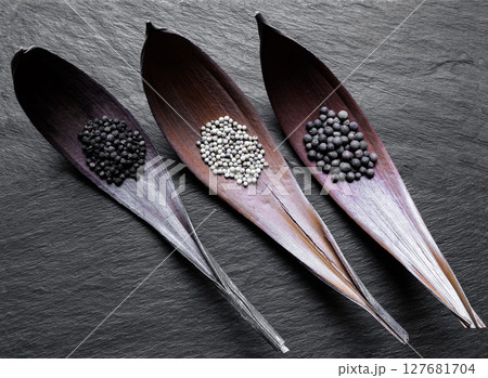Black, White and Fragrant Piles of Pepper Grains in Dry Leaf Funnels on Black Stone Background Surface 127681704