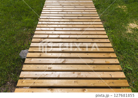 Wooden planks form an outdoor walkway surrounded by vibrant green grass Wooden planks form an outdoor walkway surrounded by vibrant green grass 127681855
