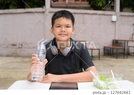 Thai boy eating salad and using wireless technology at outdoor table 127682661