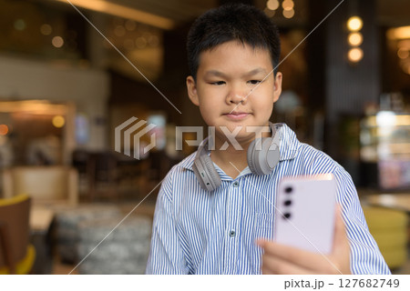 Thai boy using phone at cafe with headphones 127682749